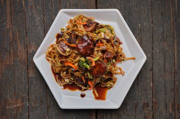 Food Fit meal containing spicy yaki udon noodles on a hexagonal white plate.