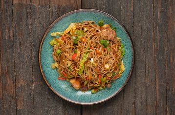 A fresh, high protein Food Fit meal containing ginger sticky glazed pork noodles on a blue plate.