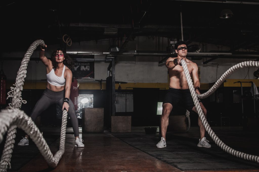 A man and woman in the gym. They're in the squat position whilst swinging ropes during a weight loss workout.