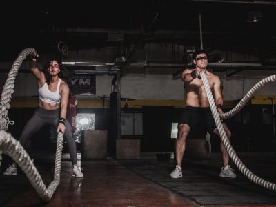 A man and woman in the gym. They're in the squat position whilst swinging ropes during a weight loss workout.